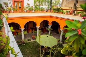 Um pátio com arcos, plantas em vasos e um guarda-sol verde.