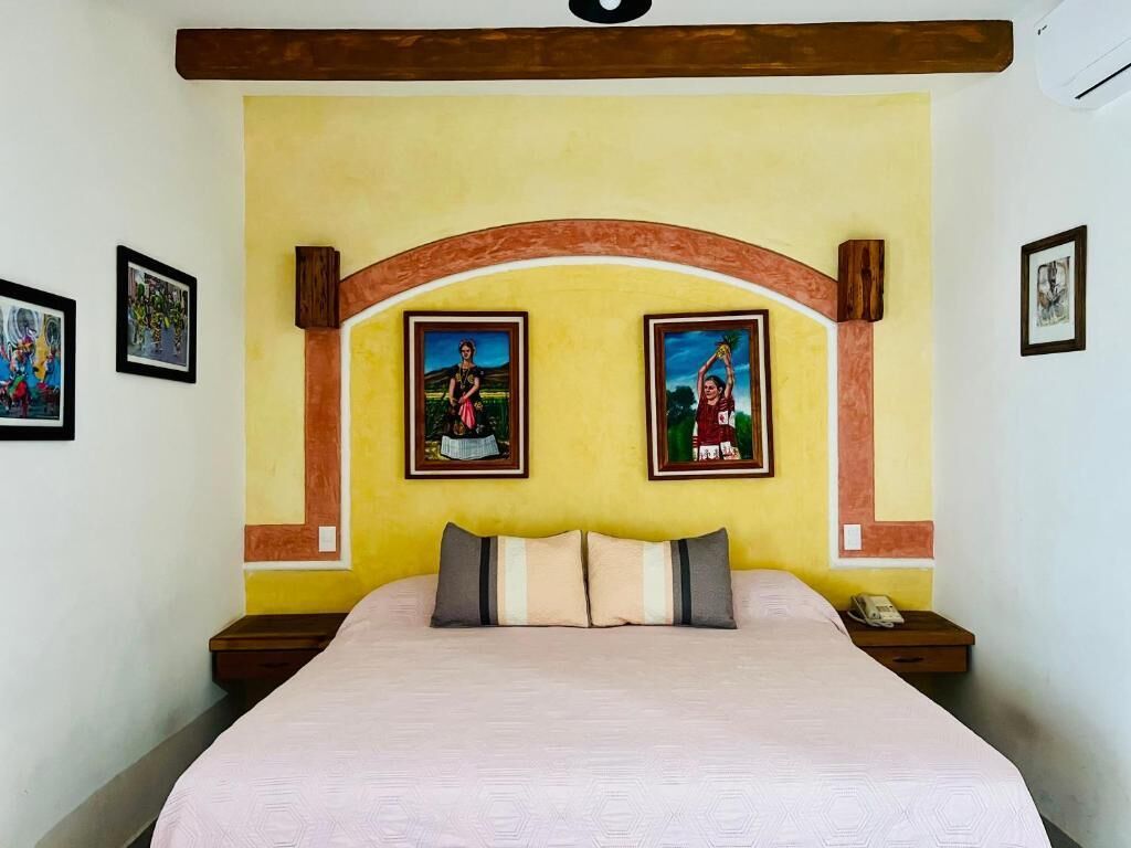 Un dormitorio con cama, dos mesitas de noche y un cabecero con arco de madera. Se observan dos cuadros en la pared.