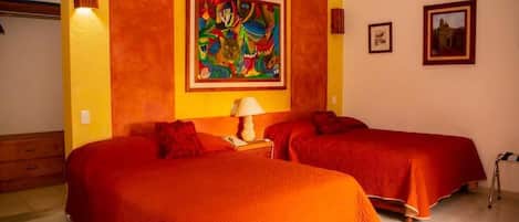 Una habitación con dos camas, un cuadro grande y colorido en la pared, y dos fotografías enmarcadas.