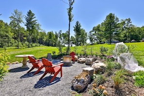 Un espace extérieur aménagé avec une table en pierre et des chaises rouges, entouré de rochers et de plantes.