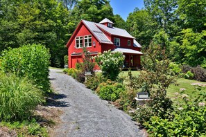 Une maison rouge avec une allée en gravier et une végétation luxuriante.