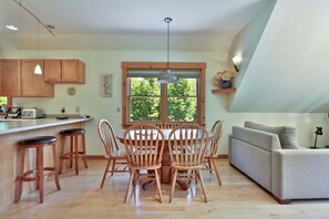 A kitchen with wooden cabinets, a dining table with chairs, a bar area, and a sofa in a living space.