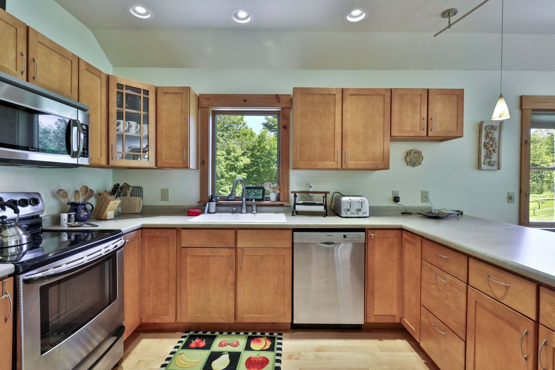 A kitchen with wooden cabinets, stainless steel appliances, a window, and a view of greenery outside.