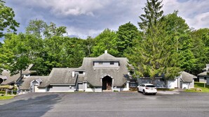 A residential area with a central building featuring a gabled roof and a prominent entrance. - Forest Hearth at The Woods | 2BR Garden Condo with Pool & Spa | Sleeps 6 (Killington)
