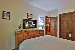 Quarto com cama, penteadeira, televisão e porta.