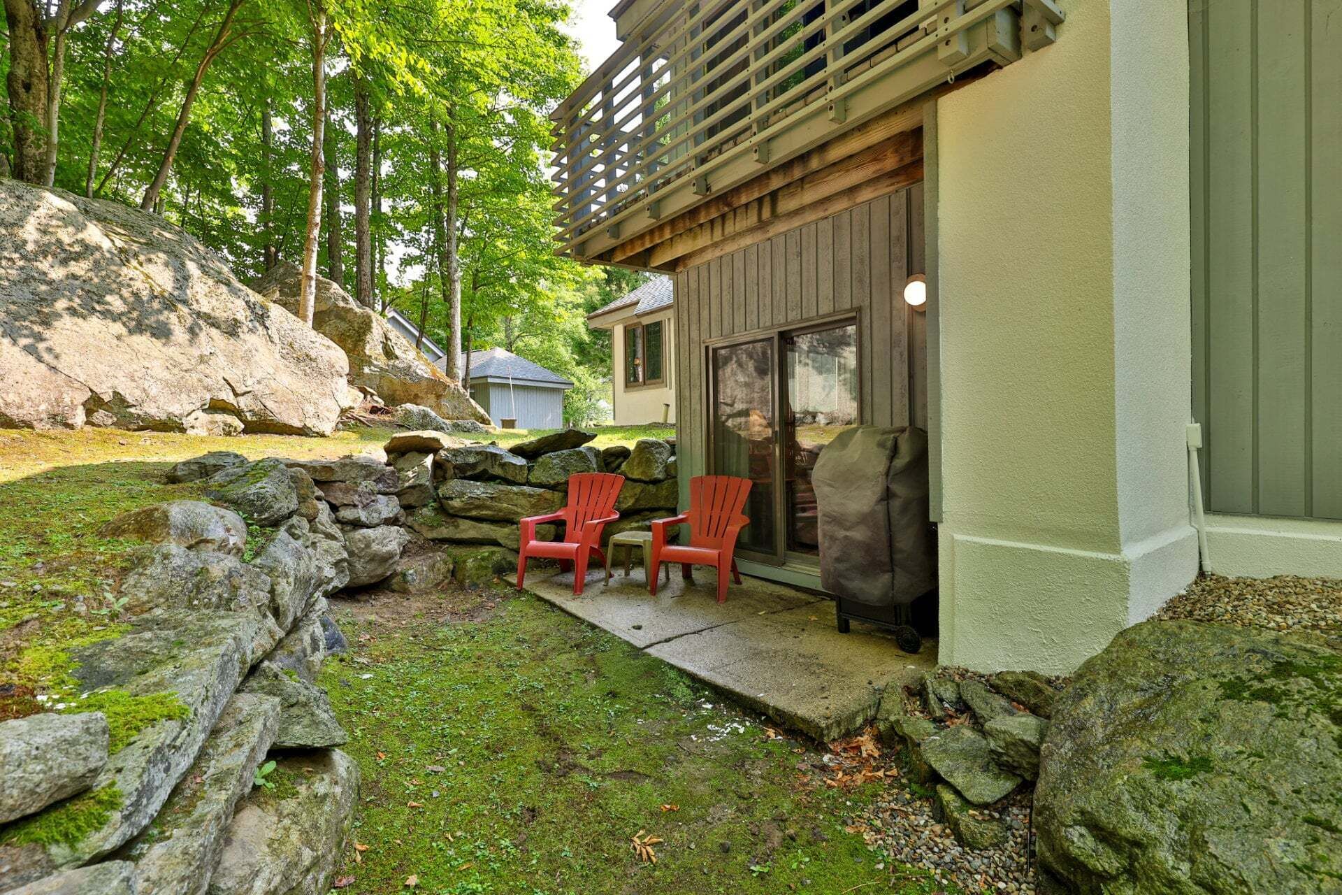 A stone wall, two red chairs, and a building with a wooden deck.