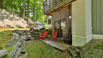 A stone wall, two red chairs, and a building with a wooden deck.