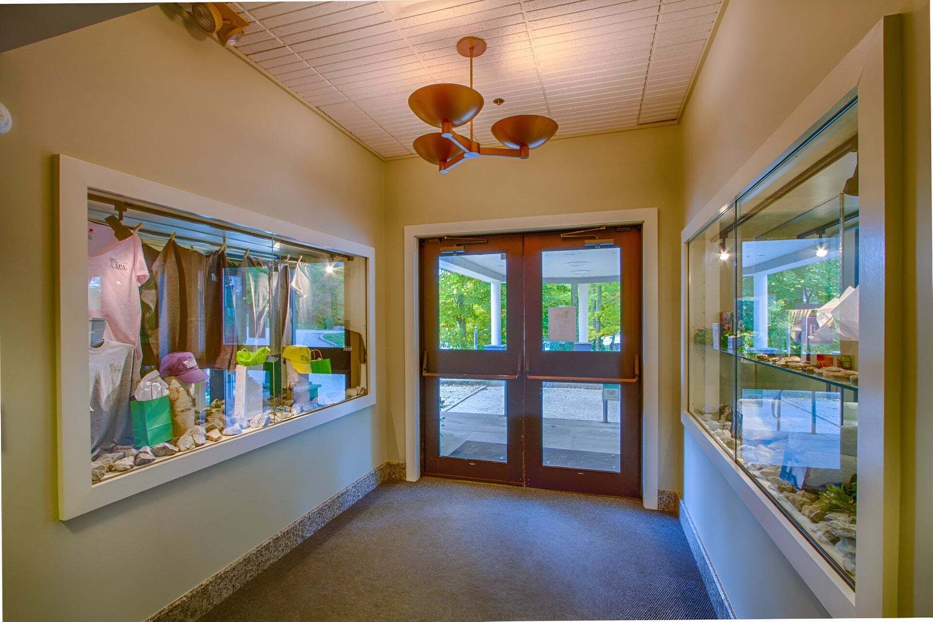A hallway with a wooden ceiling, a double door, and glass display cases on either side.