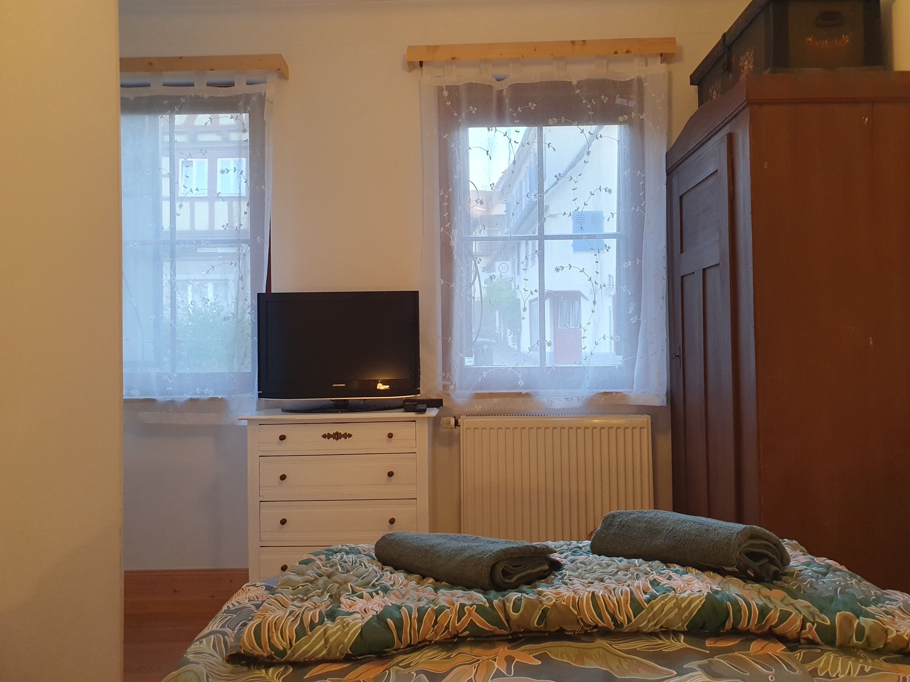 A bedroom with a bed, a TV on a dresser, and a window with a view of buildings.