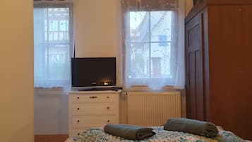 A bedroom with a bed, a TV on a dresser, and a window with a view of buildings.