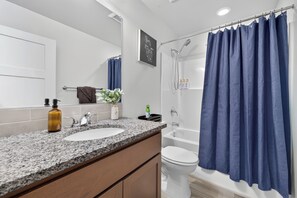 Casa de banho com lavatório branco, espelho, chuveiro e cortina de chuveiro azul.