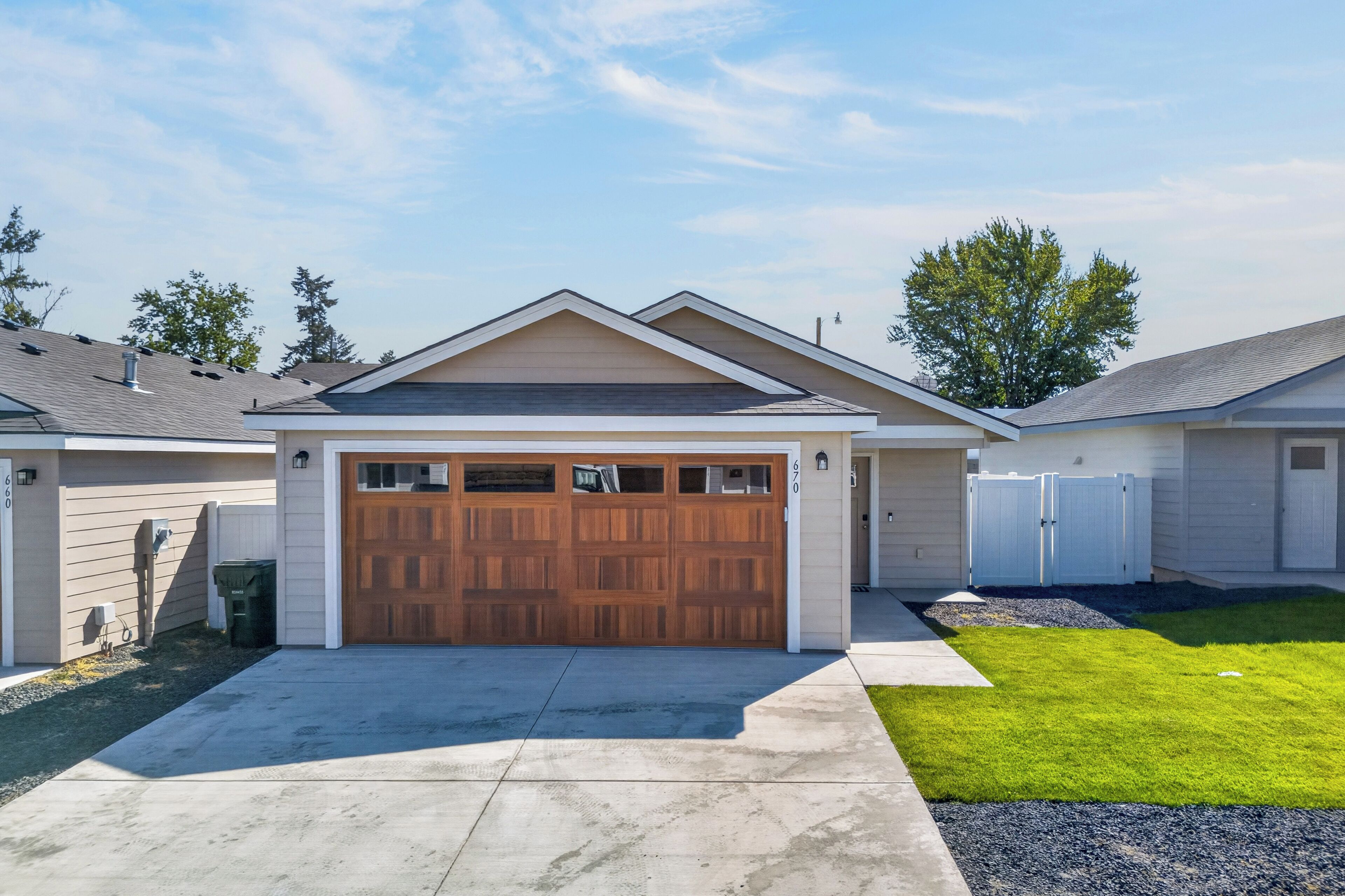 Une maison d’habitation avec un garage double, une cour avant et une clôture blanche.