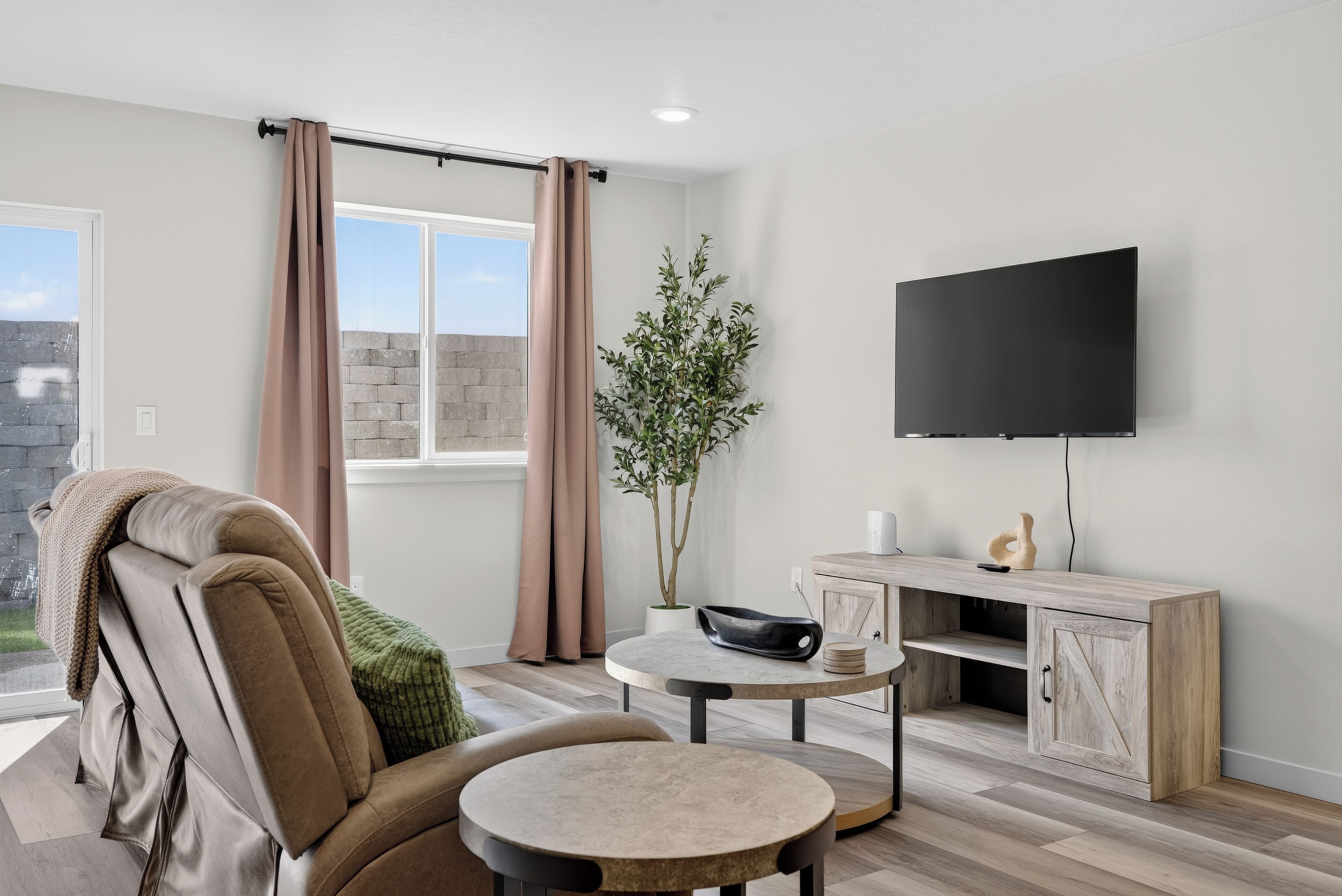 Un salon moderne avec un canapé, une petite table ronde, un téléviseur à écran plat fixé au mur et une plante en pot.