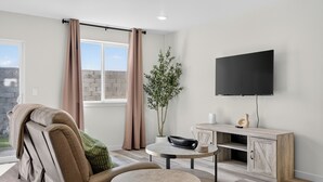 Un salon moderne avec un canapé, une petite table ronde, un téléviseur à écran plat fixé au mur et une plante en pot.