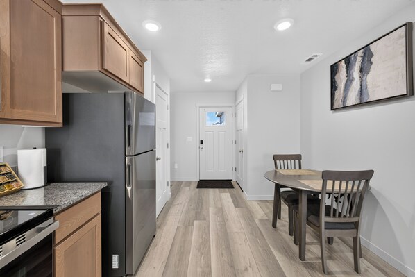 A modern kitchen with wooden cabinets, stainless steel appliances, and a dining area with a table and chairs.