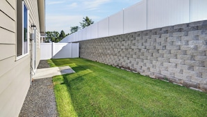 Un jardin avec une allée dallée, un mur en pierre et une clôture blanche.
