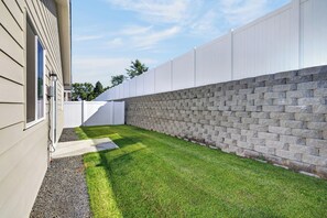 A backyard with a paved area, a stone wall, and a white fence.