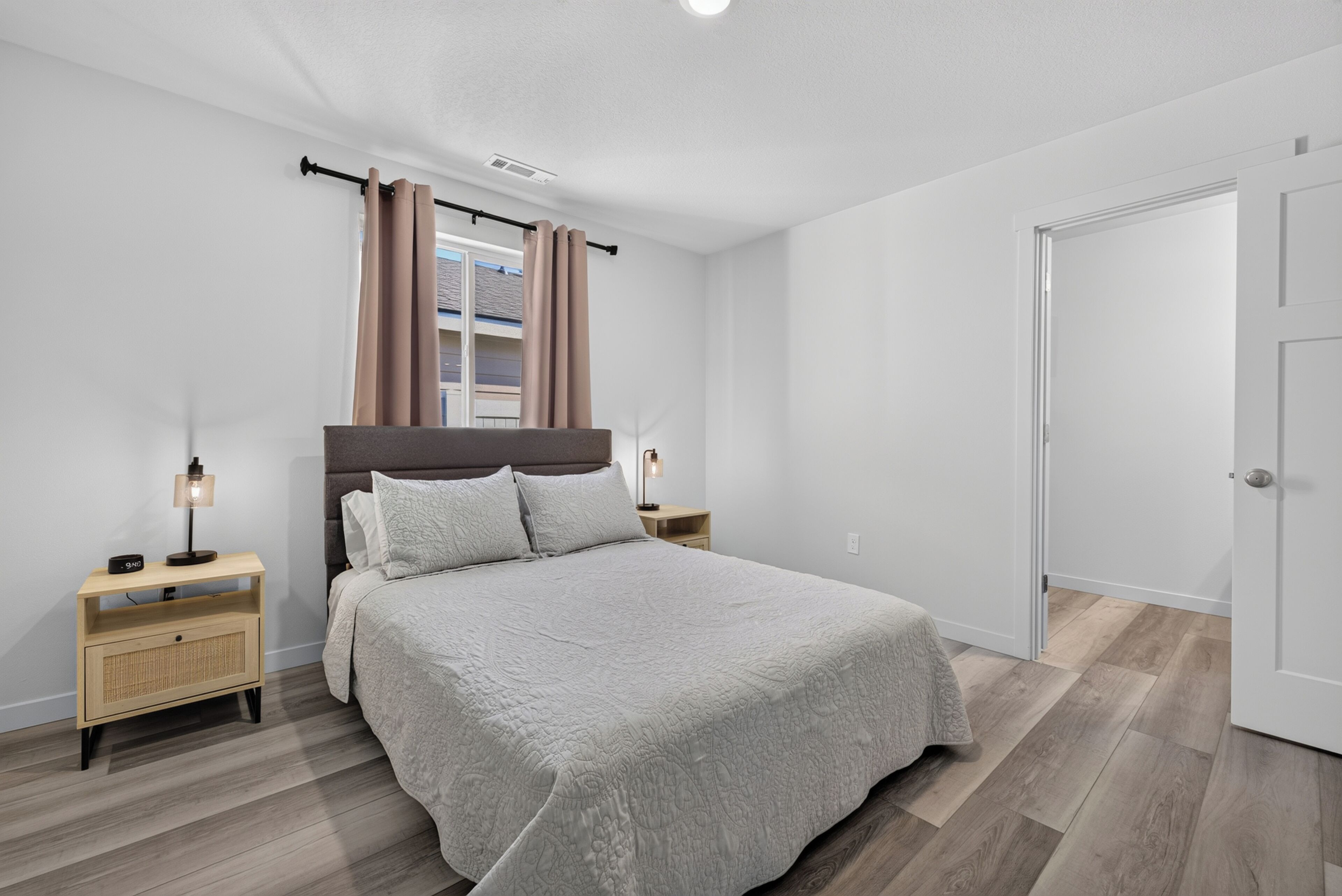 Une chambre à coucher avec un lit, des tables de chevet, une fenêtre avec des rideaux, une porte et un luminaire au plafond.