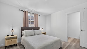 A bedroom with a bed, nightstands, a window with curtains, a door, and a ceiling light. - Proper Stay 2BD/2BA  Stanfield (Stanfield)