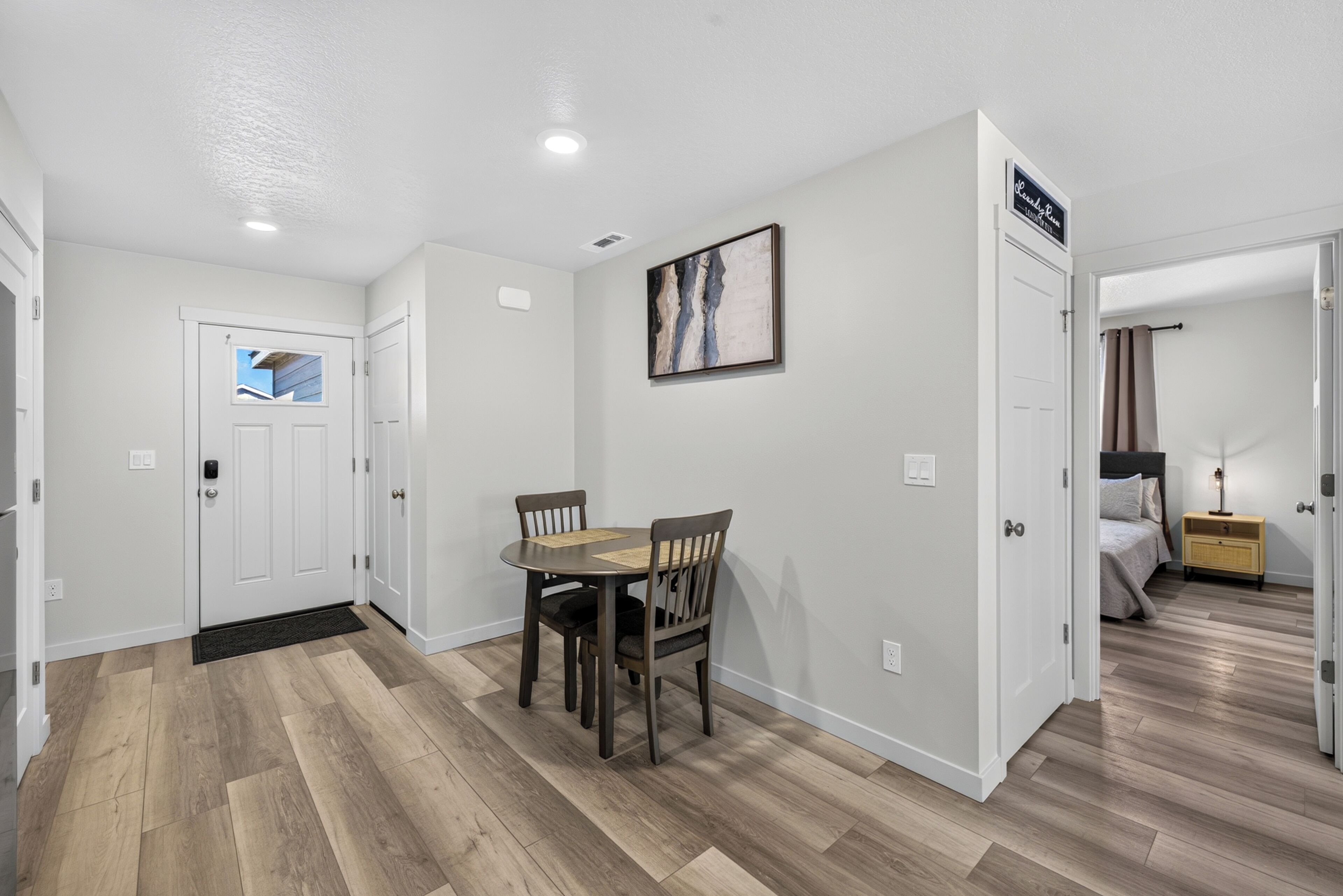 Une chambre d’hôtel avec un plancher en bois, une table à manger avec des chaises, un lit et une table de chevet avec une lampe.