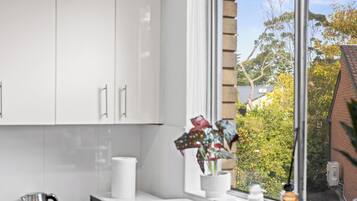 A modern kitchen with white cabinets, a kettle, and a window with a view of trees and a building.