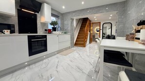 A modern kitchen with a built-in oven, a microwave, and a coffee maker. There is a staircase leading to a dining area with a table and chairs. - Brand New! (Cardiff)