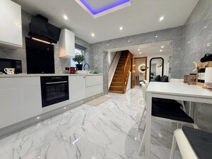Eine moderne Küche mit Backofen, Mikrowelle und Kaffeemaschine. Eine Treppe führt zu einem Essbereich mit Tisch und Stühlen.