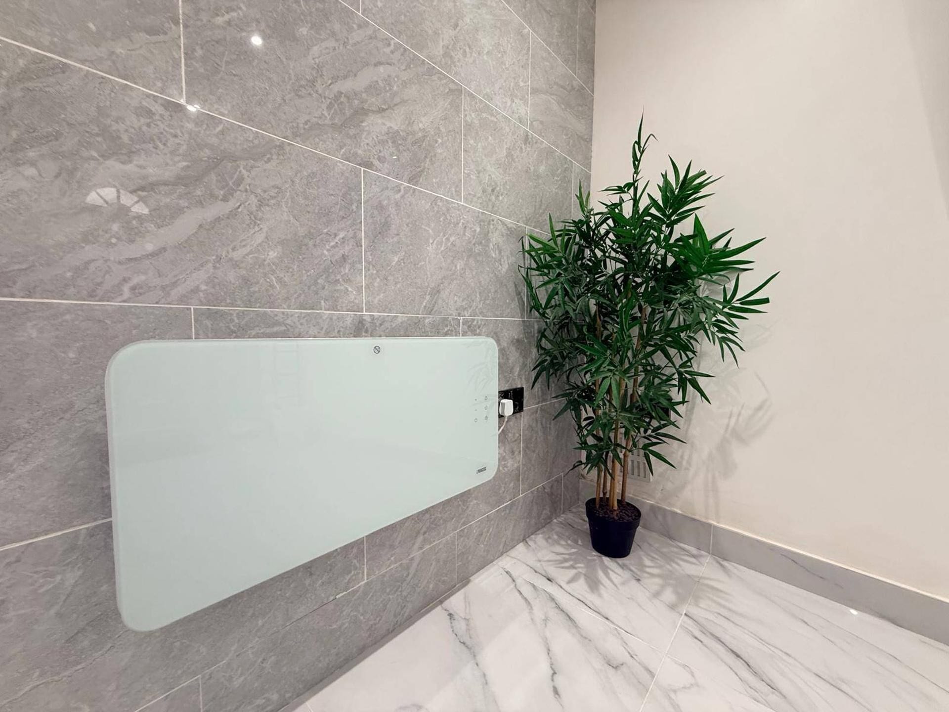 A bathroom with a glass shower enclosure, a potted plant, and marble tiles.