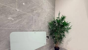 A bathroom with a glass shower enclosure, a potted plant, and marble tiles.