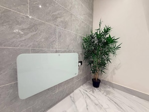 Un baño con cabina de ducha de vidrio, una planta en maceta y baldosas de mármol.