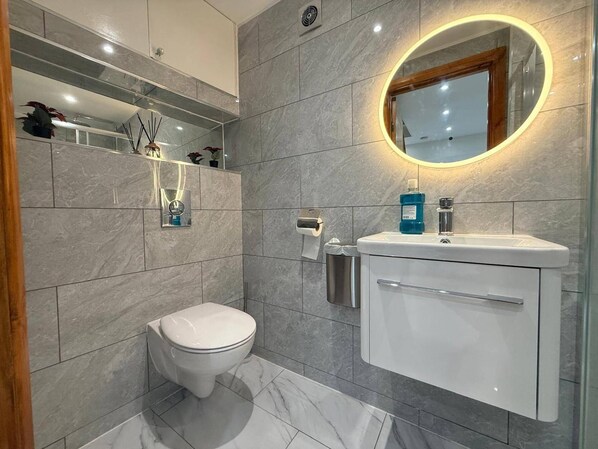 A modern bathroom with a toilet, sink, and mirror. - Brand New! (Cardiff)