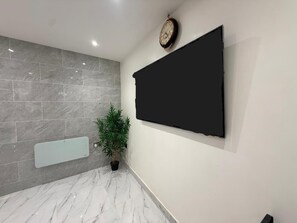 A modern bathroom with a large mirror, a wall-mounted TV, and a potted plant. - Brand New! (Cardiff)