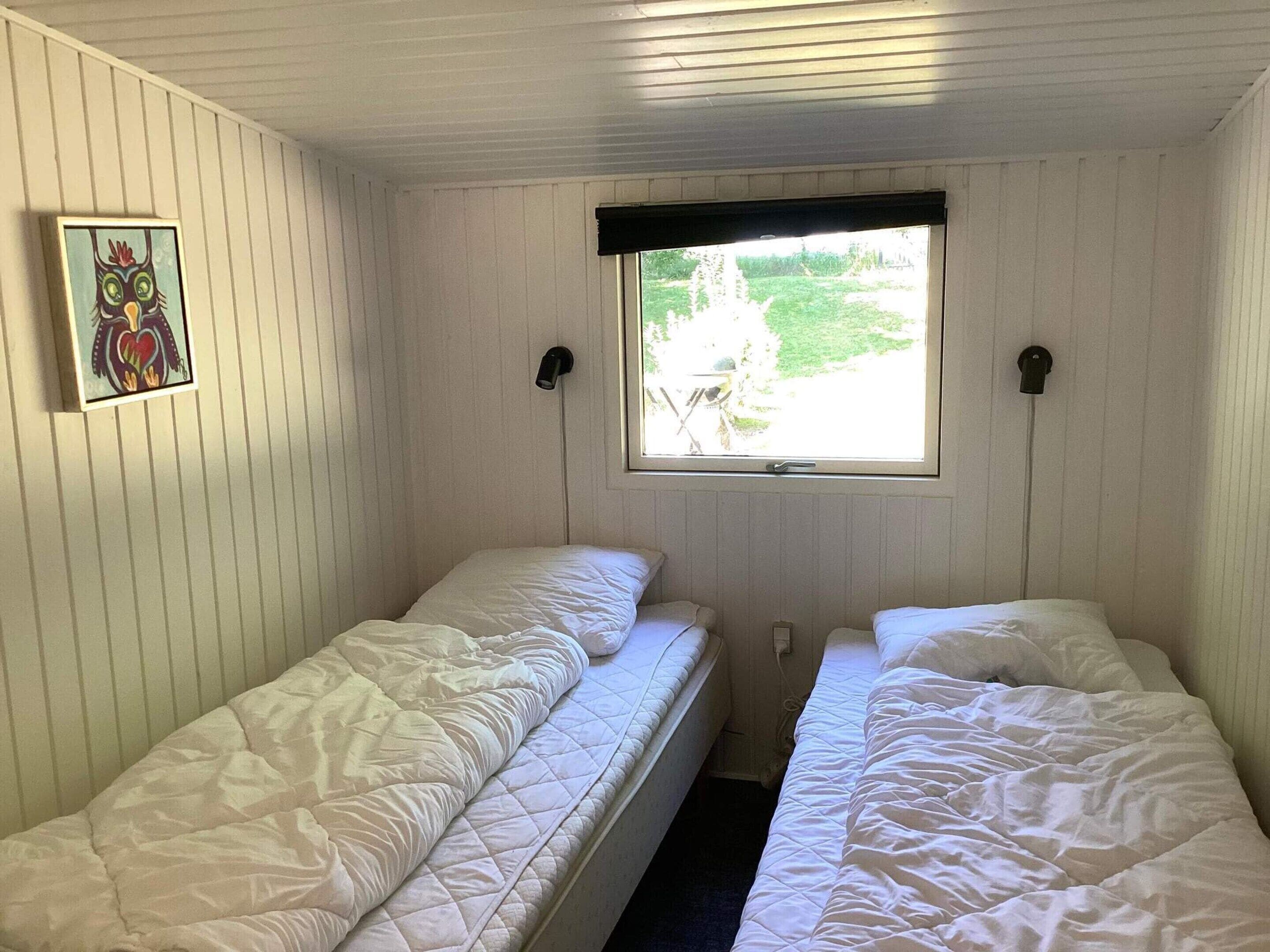 Une chambre avec deux lits simples, une fenêtre donnant sur un espace verdoyant et un luminaire fixé au mur.