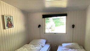 Een kamer met twee eenpersoonsbedden, een raam met uitzicht op groen en een wandlamp.