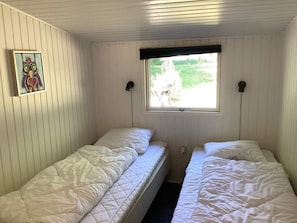 Ein Zimmer mit zwei Einzelbetten, einem Fenster mit Blick auf Grünflächen und einer Wandleuchte.
