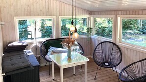 Een kamer met een houten plafond, een tafel met stoelen, een klok en ramen met uitzicht op groen.