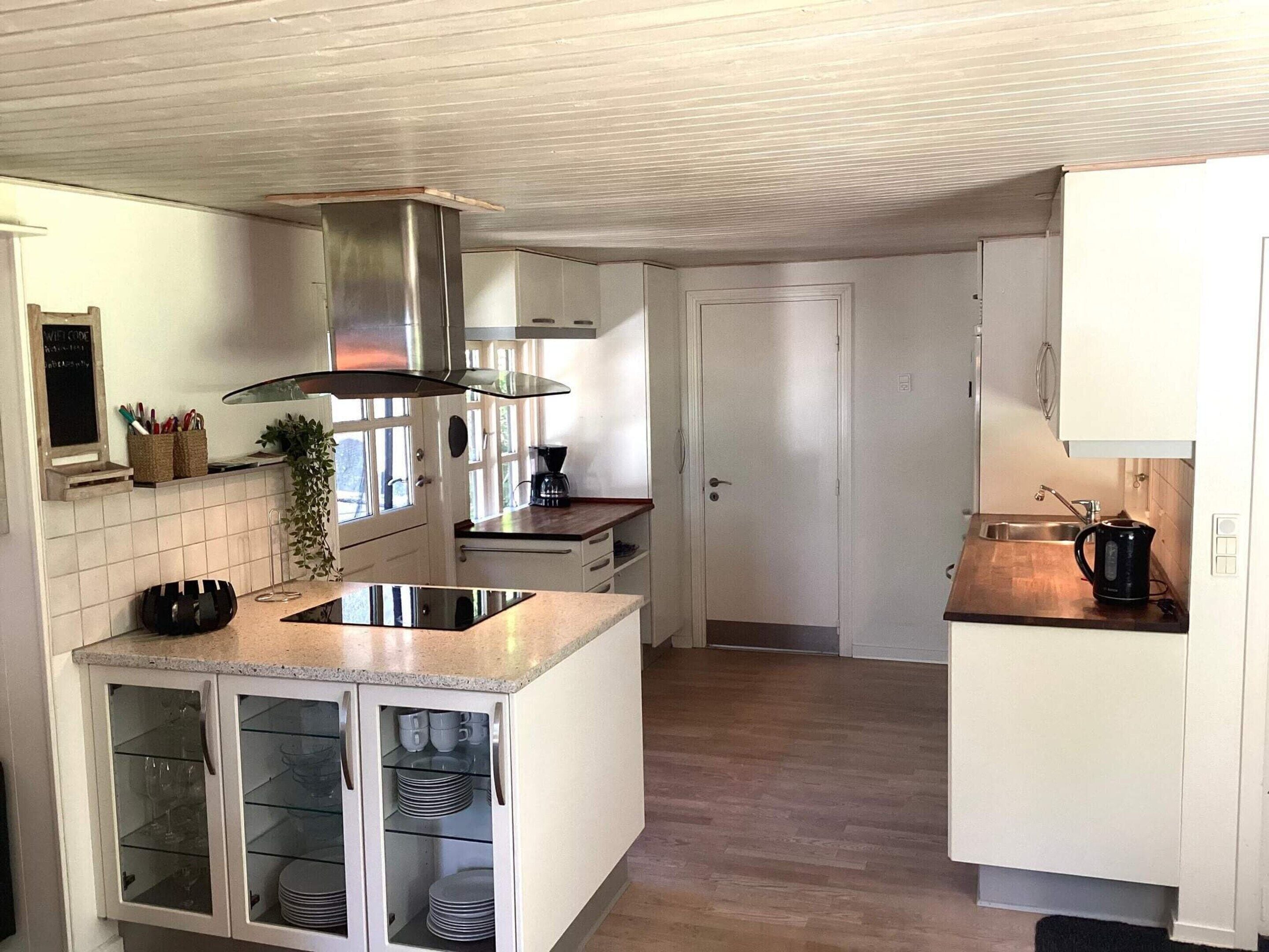 A kitchen with white cabinets, a stainless steel range hood, a coffee maker, and a sink.