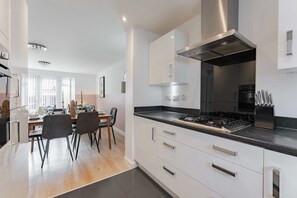 Eine moderne Küche mit Gaskochfeld, Edelstahlmöbeln und einem Essbereich mit Tisch und Stühlen.