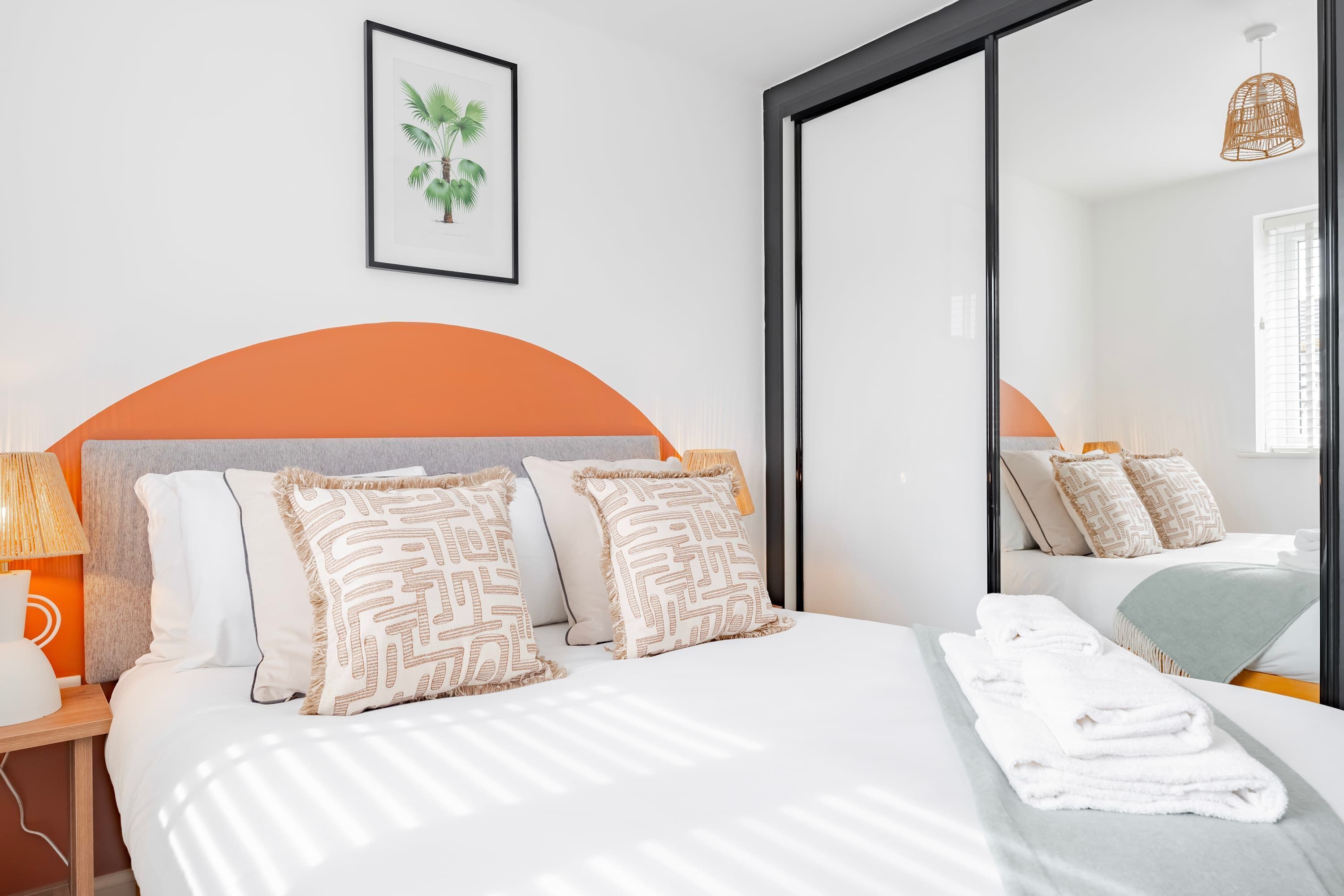 A hotel room with a bed, pillows, a lamp, a framed picture, and a mirror.