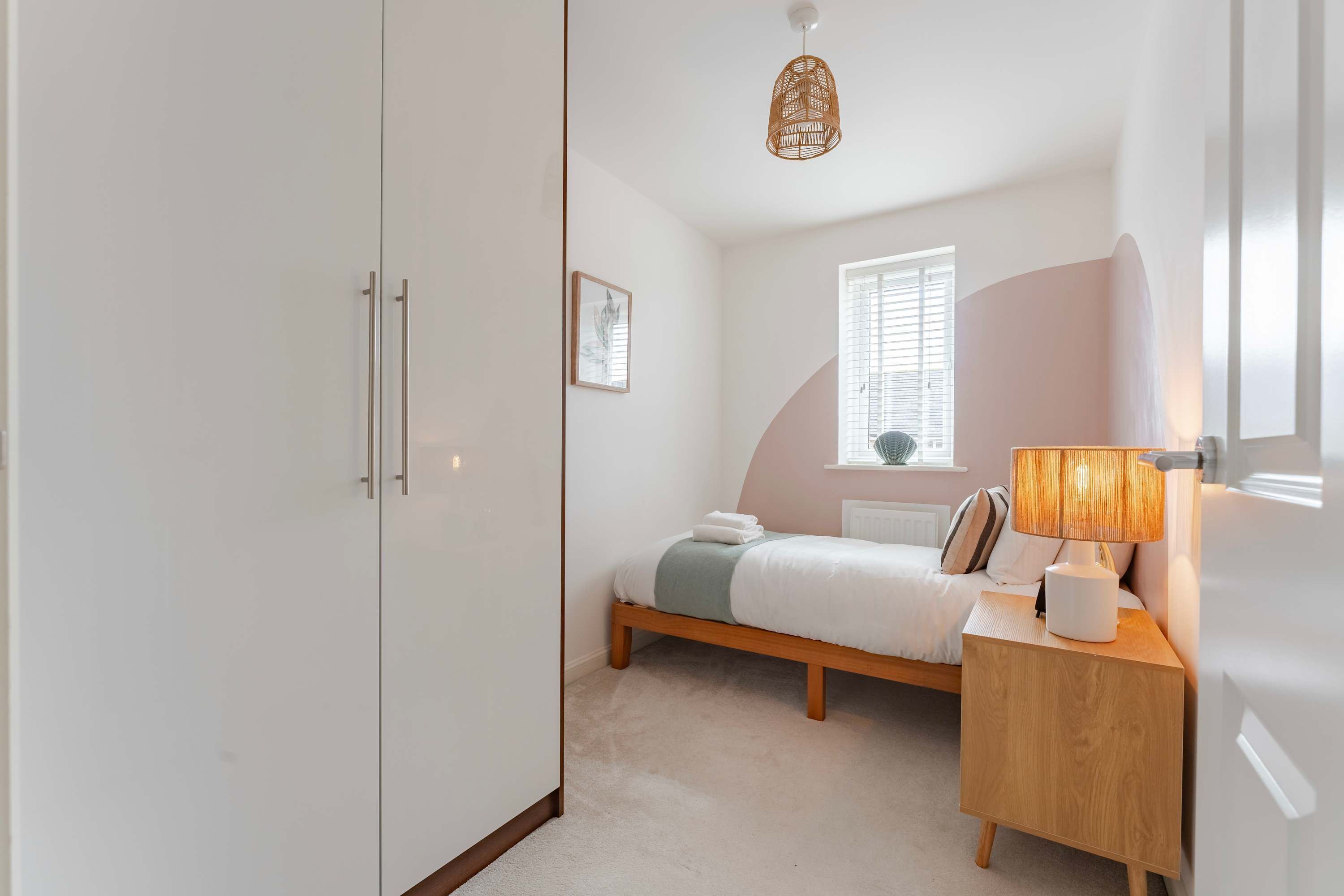 Um quarto com cama, mesa de cabeceira, luminária, janela e guarda-roupa.