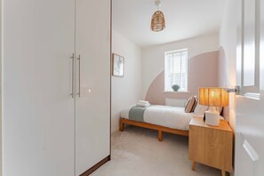Ein Schlafzimmer mit Bett, Nachttisch, Lampe, Fenster und Kleiderschrank.