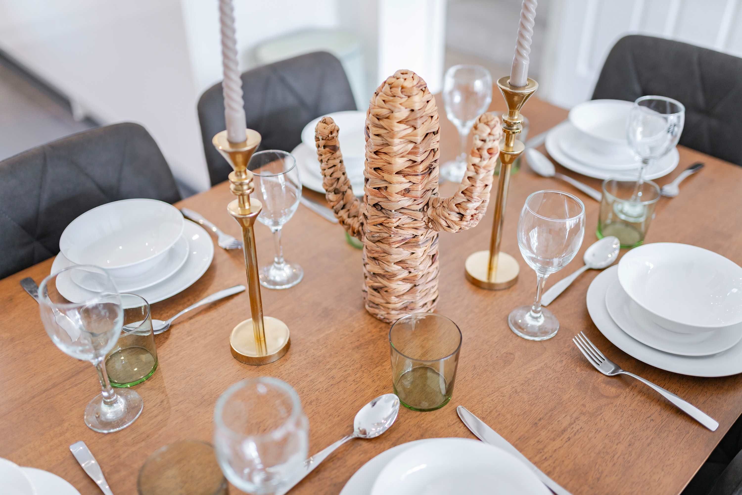 A dining table set with white plates, cutlery, and glasses, with a woven centerpiece.