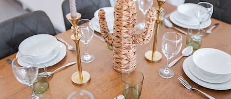 A dining table set with white plates, cutlery, and glasses, with a woven centerpiece.