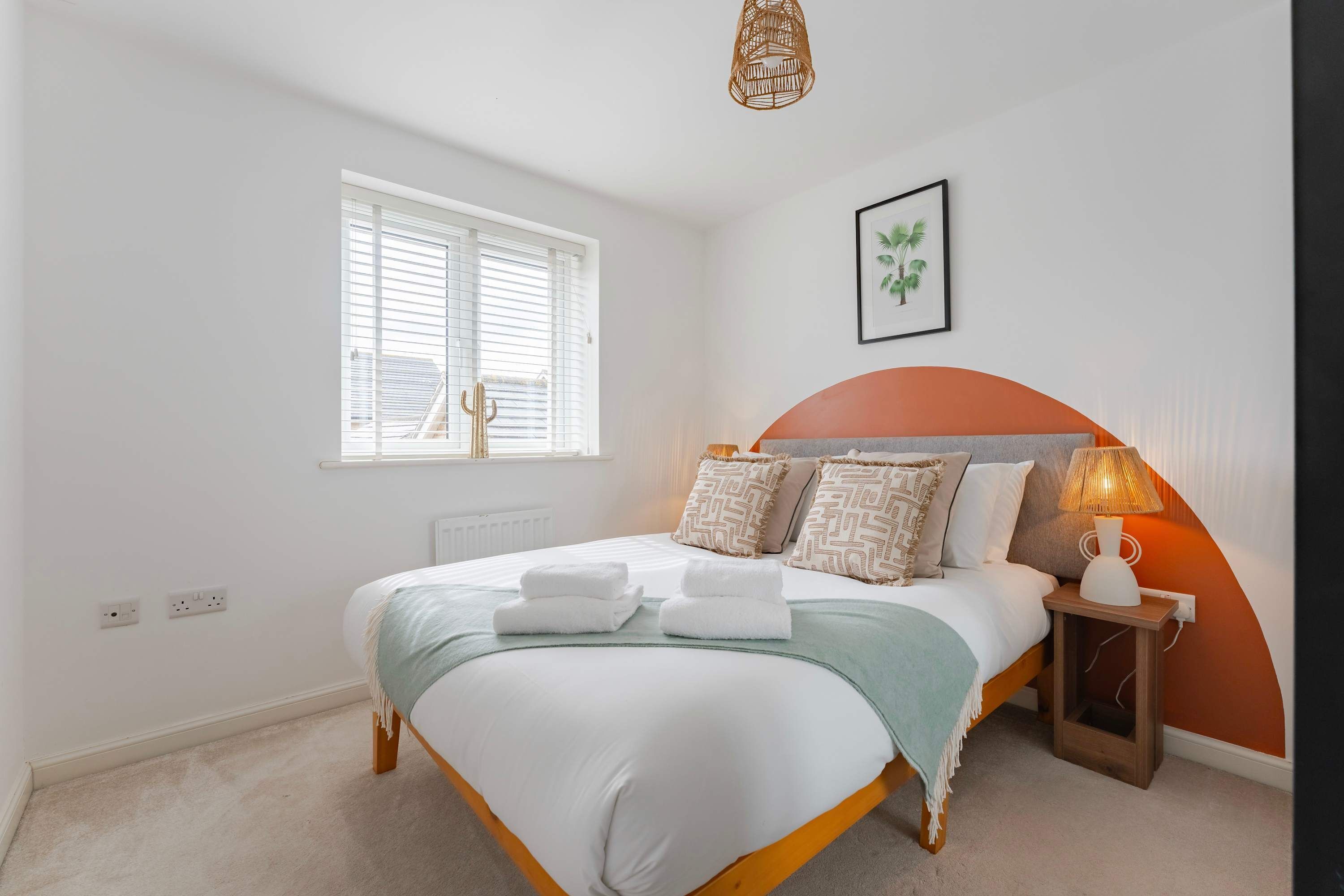 Une chambre à coucher avec un lit, une table de chevet, une lampe et une fenêtre avec des stores.