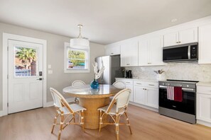 A kitchen with white cabinets, a stainless steel oven, a microwave, and a dining area with wicker chairs and a round table. - 3BR Old Village Retreat - Extended Stay w/ Pool (Mount Pleasant)