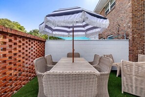 A patio with a table and chairs, a striped umbrella, and a brick wall. - 3BR Old Village Retreat - Extended Stay w/ Pool (Mount Pleasant)