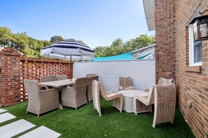 Een terras met rieten meubilair, een tafel en een gestreepte parasol.