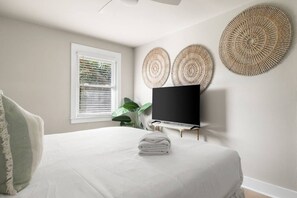 A bedroom with a bed, a television on a stand, and two wall-mounted decorative items. - 3BR Old Village Retreat - Extended Stay w/ Pool (Mount Pleasant)