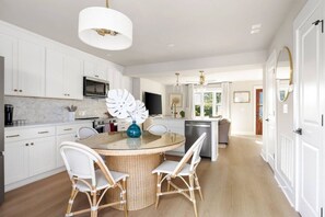 A modern kitchen with white cabinetry, a round dining table with wicker chairs, and a decorative white vase. - 3BR Old Village Retreat - Extended Stay w/ Pool (Mount Pleasant)