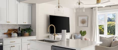 A modern kitchen with white cabinetry, a central island, a built-in dishwasher, and pendant lighting.